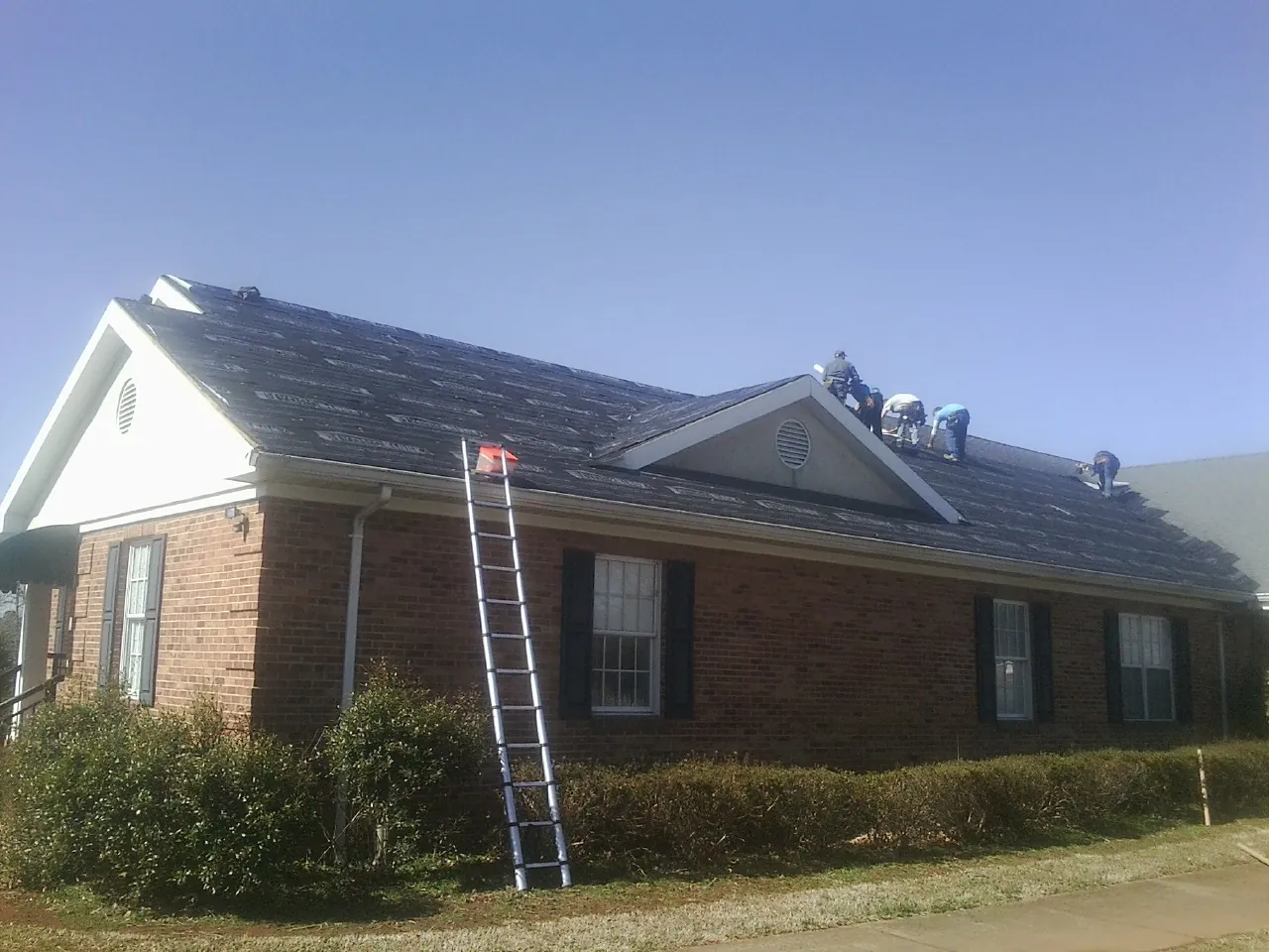 Crew tearing shingles off a brick ranch roof with a ladder set — Emergency Roof Repair work by our crew in Dilworth