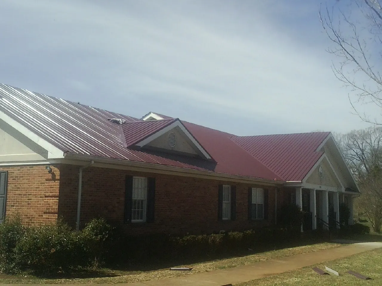 Red metal roof with gabled entries on a long brick building, from a Hail Damage Roof Repair job in Dilworth