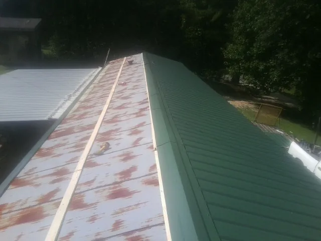 Old rusted panels beside newly installed green metal roofing — Wind Damage Roof Repair by Roofing Brothers in Dilworth
