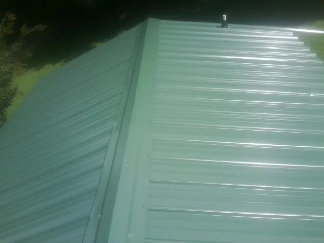 New green metal panels meeting at the ridge of a roof — Flat Roof Repair work by our crew in Dilworth