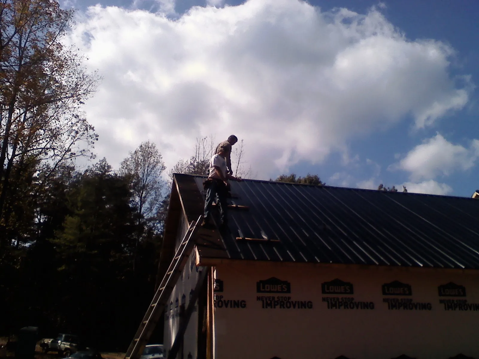 Roofer fastening dark metal panels high against a cloudy sky, from a Roof Inspection job in Dilworth